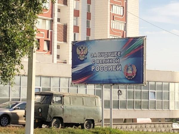 Billboard sign saying For Future with Great Russia, with a building in the background and an old van under it.