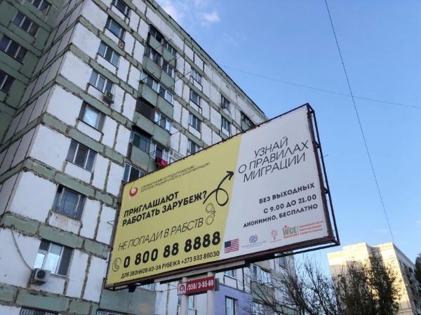 Billboard sign in front of a building with information about work, migration and a helpline number.