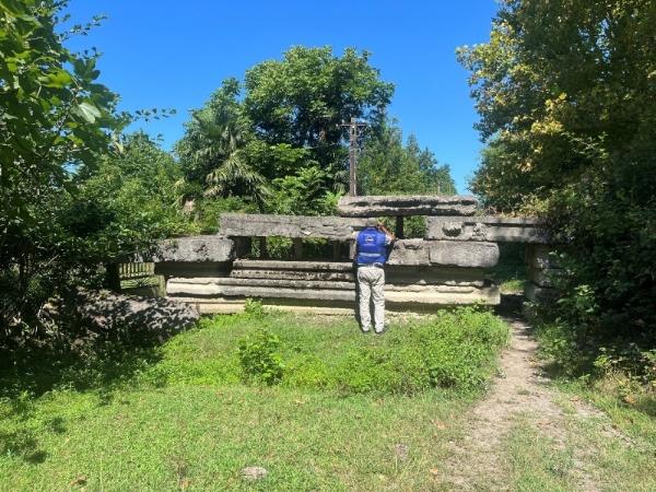 EUPM officer shown peeking over an improvised concrete wall barricade in a forest area.