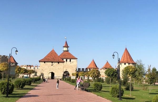 Fortress in white stone with red roofs and a park area in front.
