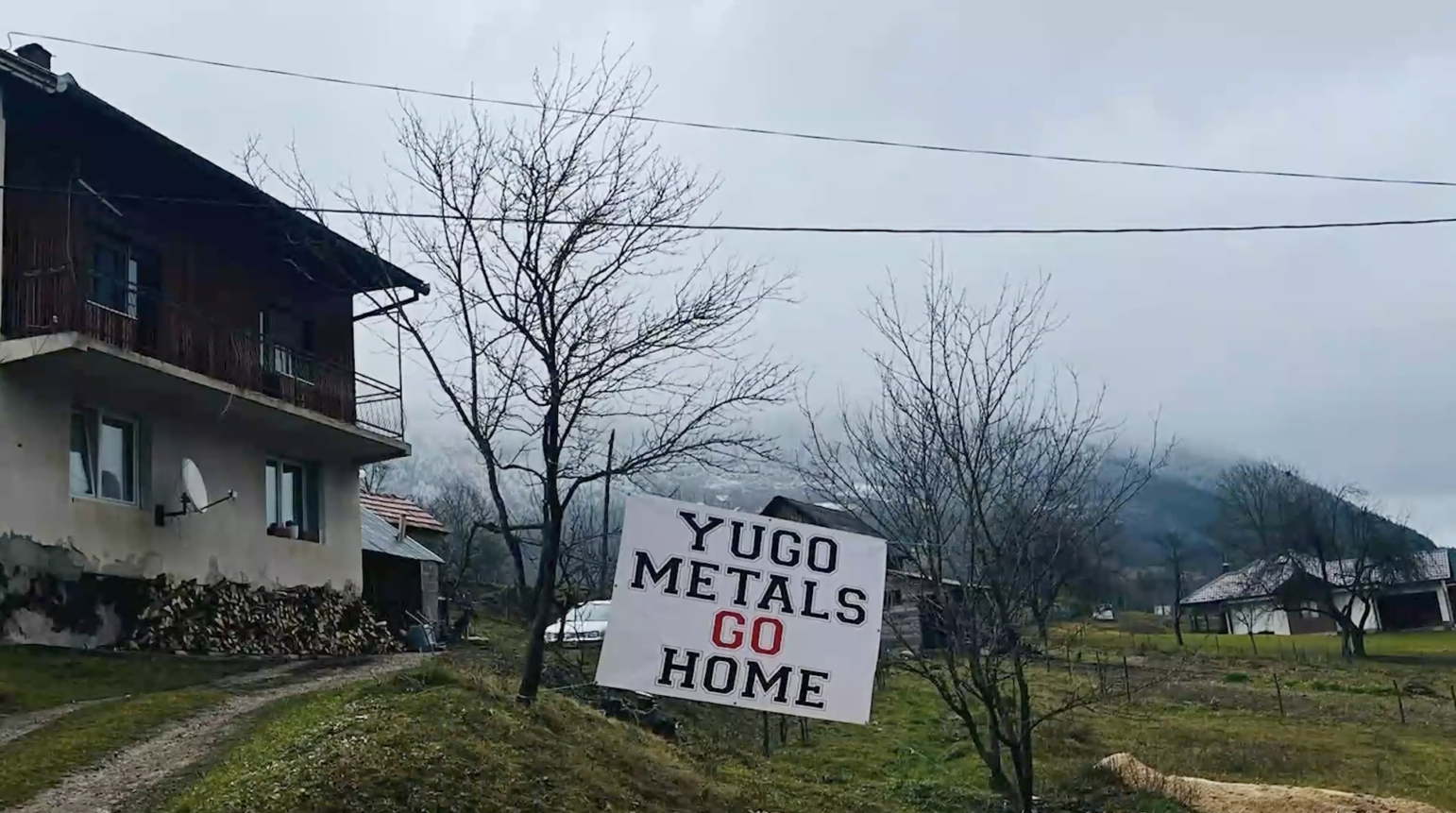 Protest sign in front of a house on a field saying Yugo Metals Go Home.